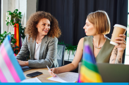 two woman in a workplace with a pride flag in the foreground.